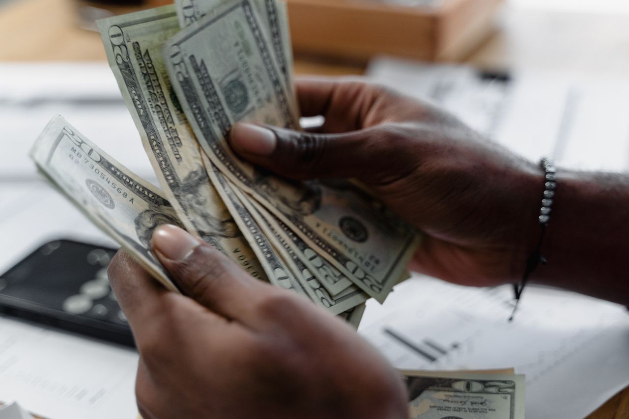 about-us-img Detailed image of hands counting US dollar bills on a desk, emphasizing finance and budgeting.